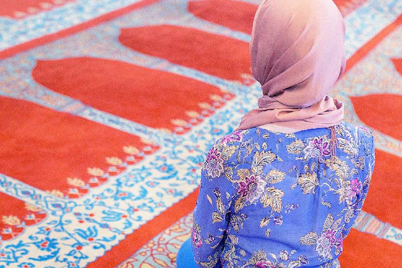 A hijabi woman kneeling on a prayer rug