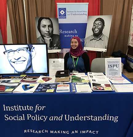 A young woman wearing a hijab behind a booth filled with reports