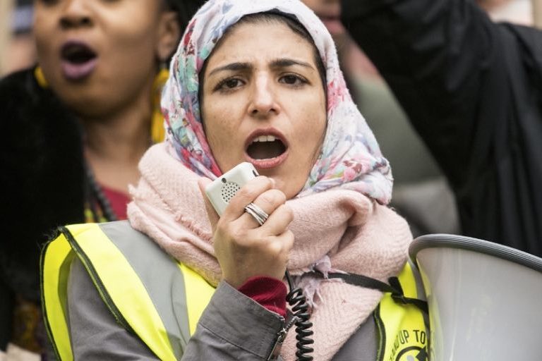 A woman wearing a hijab speaks in to a megaphone at a protest