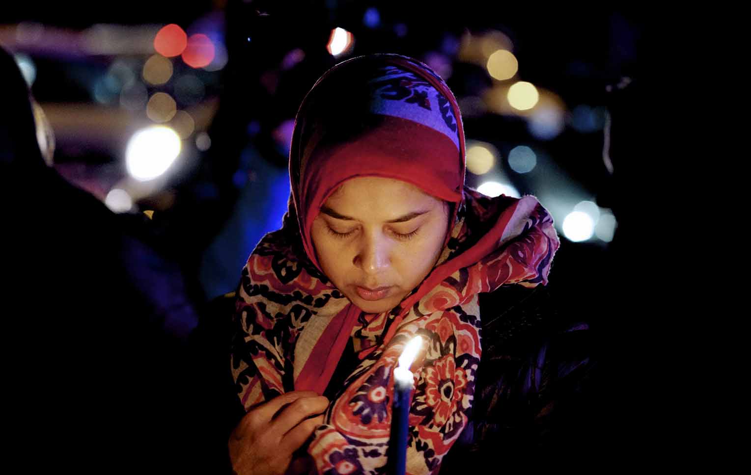 A Muslim woman at a vigil holds a candle and bows her head