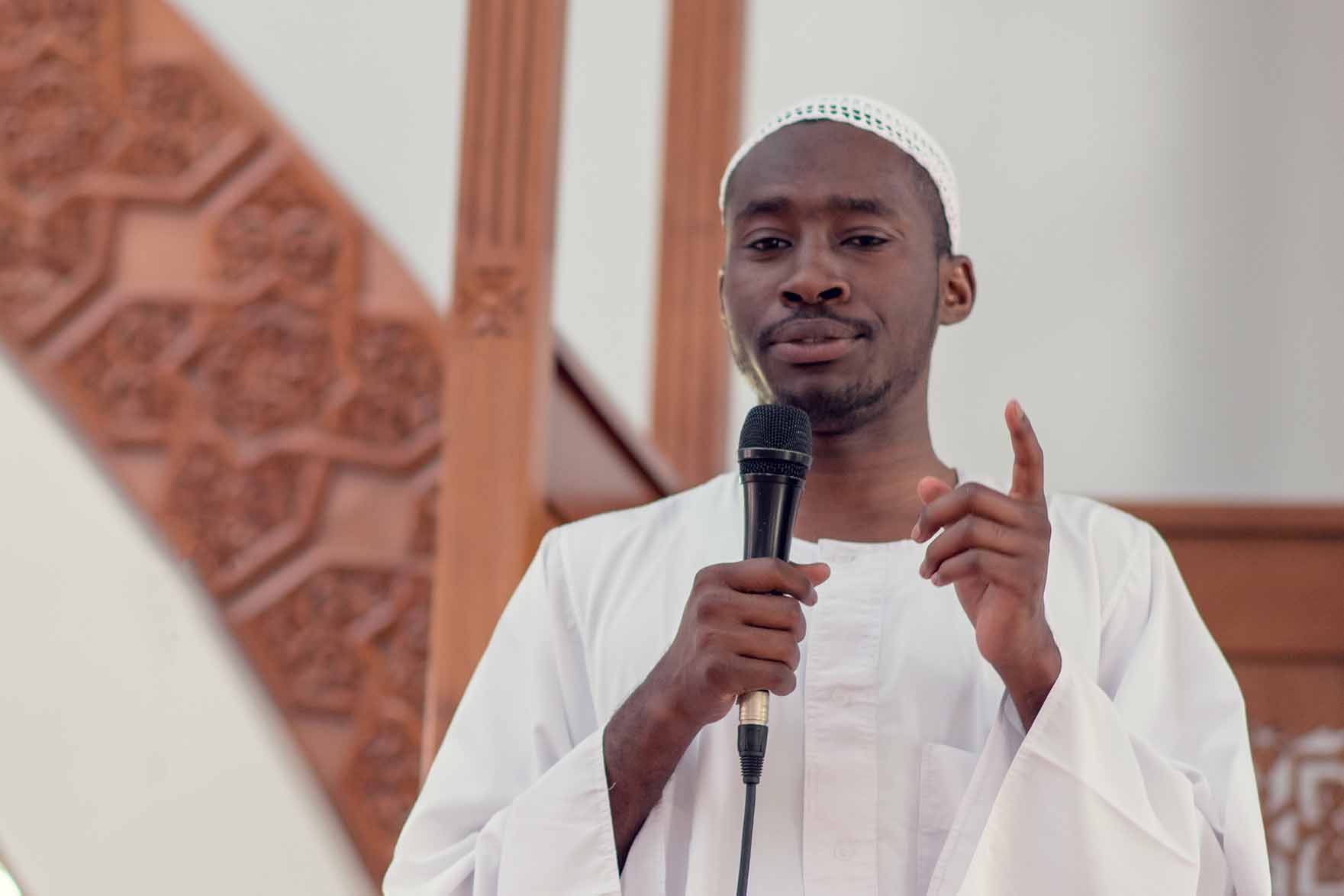 An imam holding a microphone speaking to his congregation