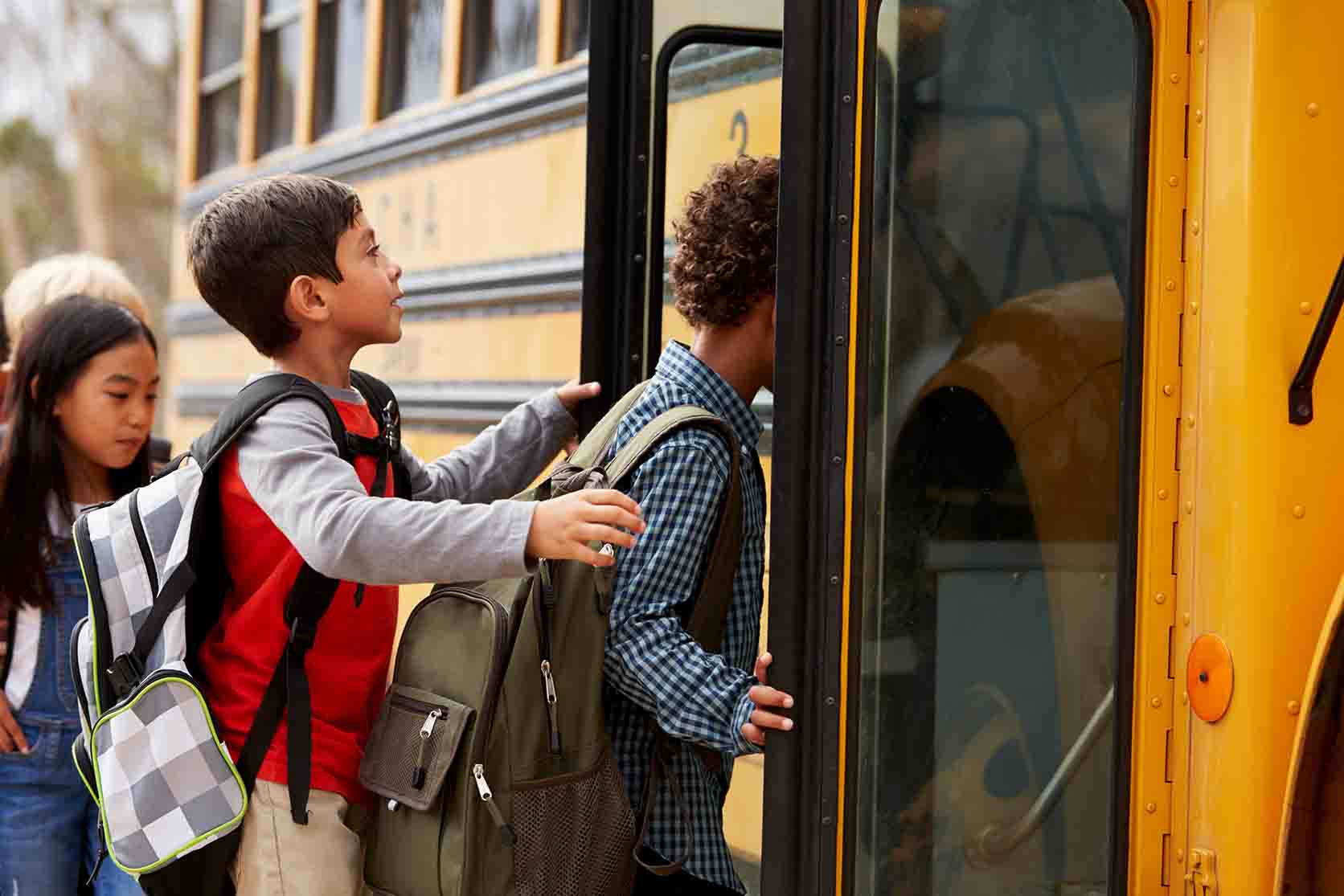 three young students boarding a school bus