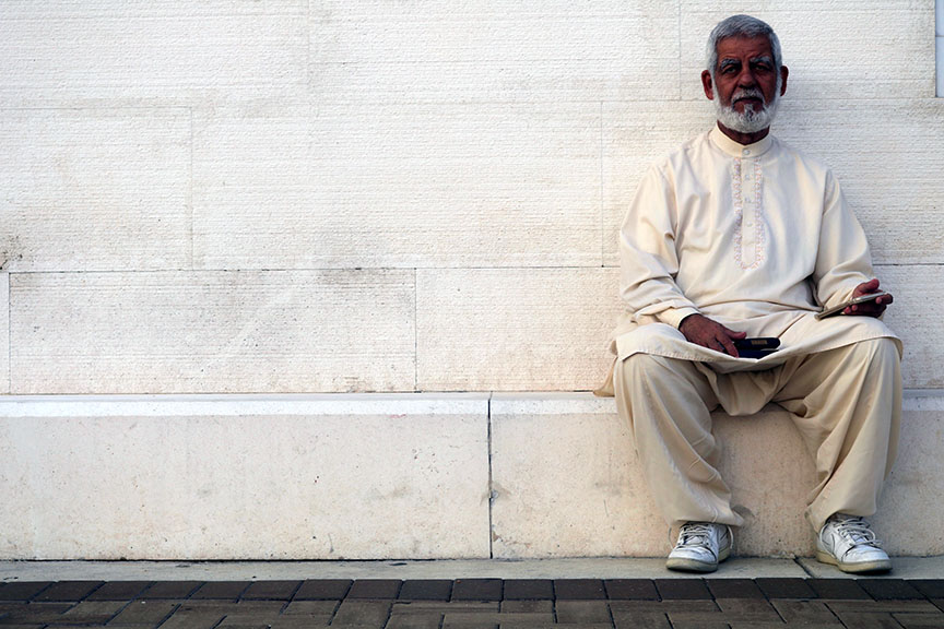 An older man with a beard sitting outside a mosque