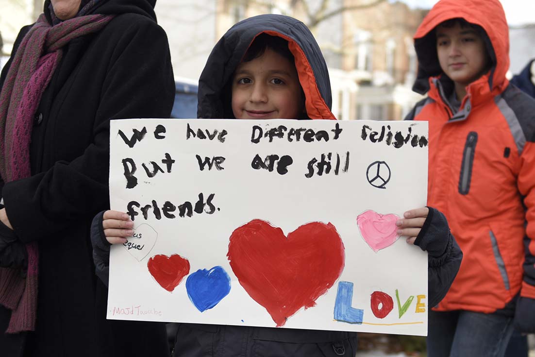A young boy at a rally carries a sign that says "we have different religions, but we are still friends"