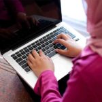 A girl in hijab typing on a laptop