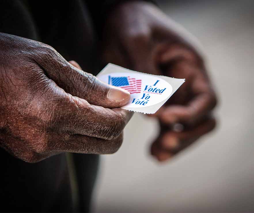 An elderly African American man holds his “I voted” sticker after he cast his ballot
