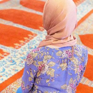 Woman wearing an orange hijab kneeling in a mosque