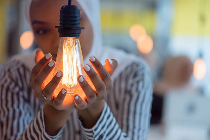 A woman wearing a white hijab cradles a lit light bulb in her hands