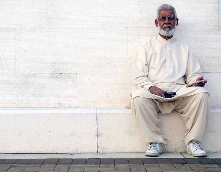 An older man with a beard sitting outside a mosque