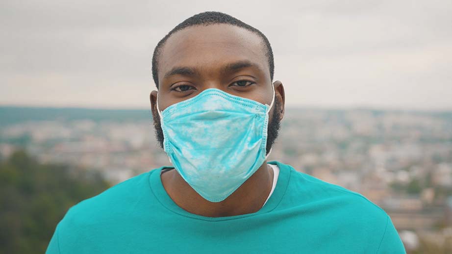 Portrait of man wearing protective face mask looking straight standing on the hilltop above city
