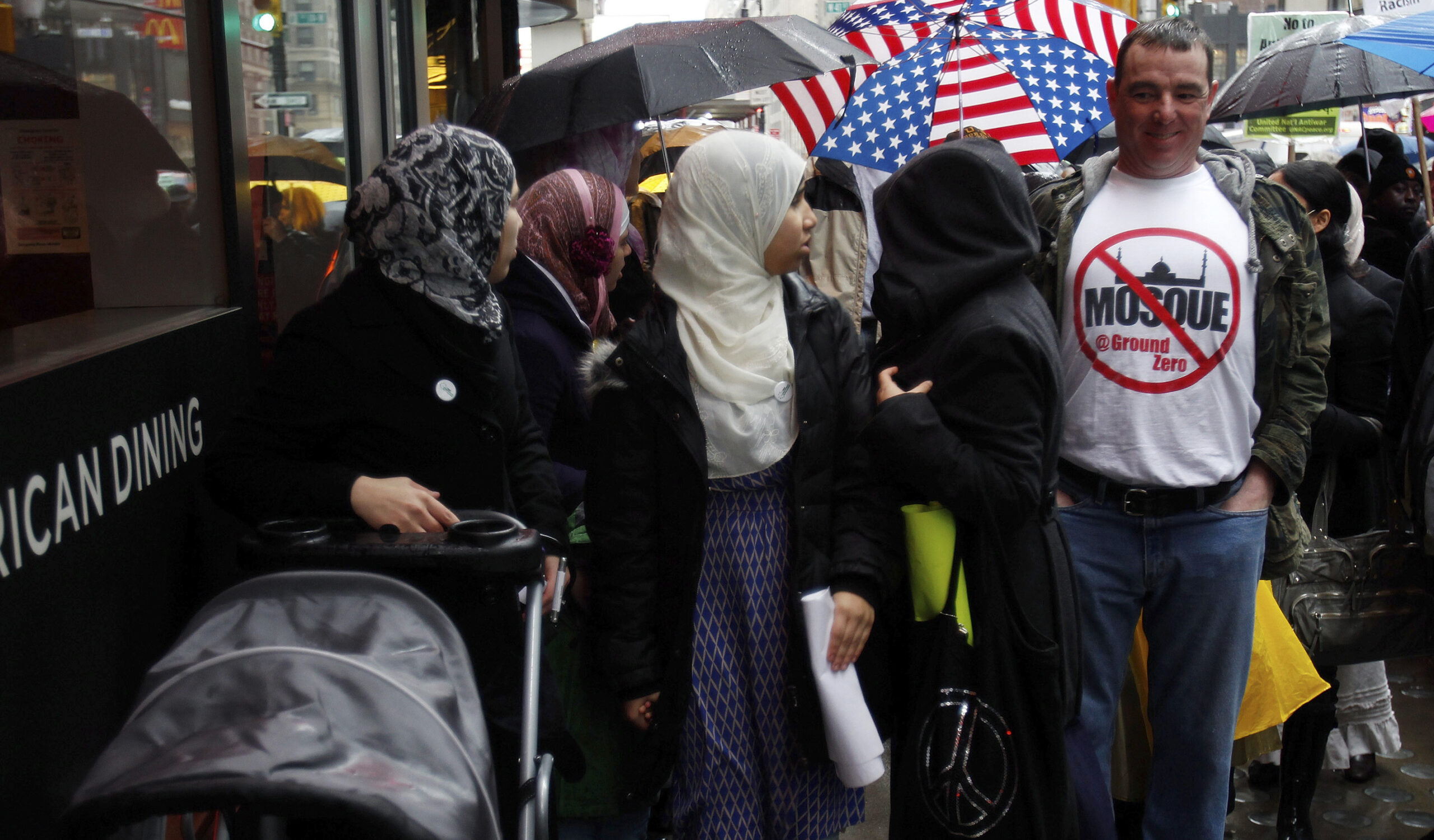 Muslim women look at a man in a T-shirt showing his opposition to proposal of building a mosque near World Trade Center site, near the "Today, I Am A Muslim, Too" rally in New York City