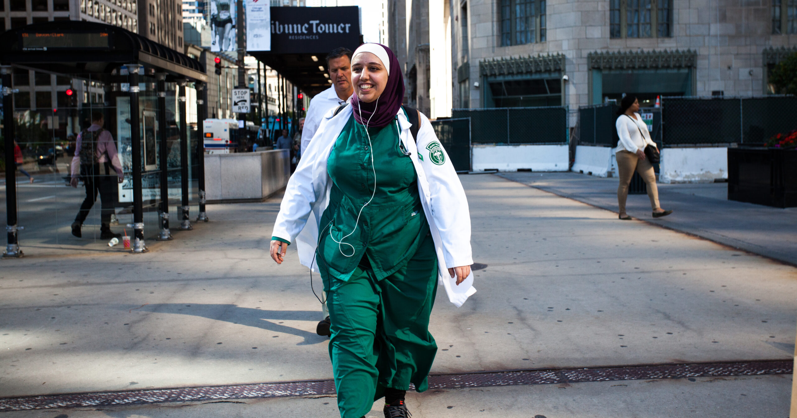 A woman wearing a hijab and medical scrubs crosses the street