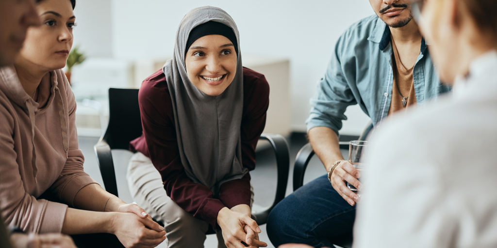 A young woman wearing a hijab smiles while engaged in a small group conversation