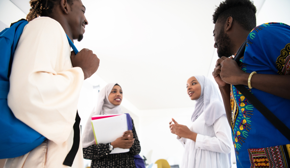 Two young women wearing hijabs and two young men smile having a conversation with school supplies.