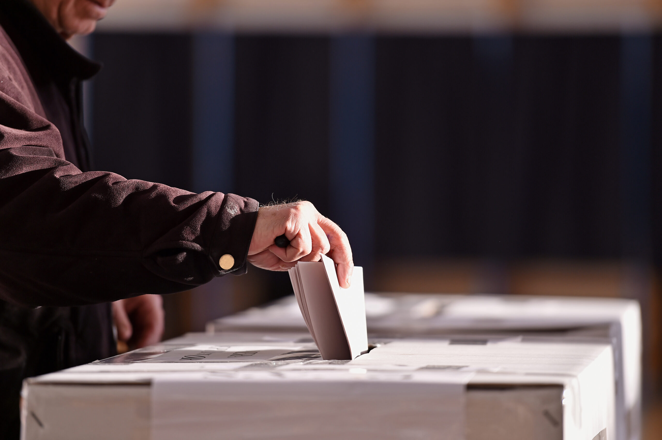 A hand casts a voting ballot into a box.