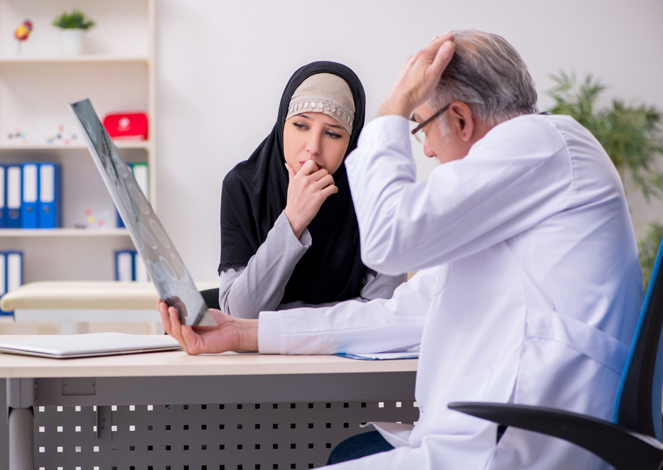 A concerned woman wearing a hijab looks at a scan held by an older male doctor.